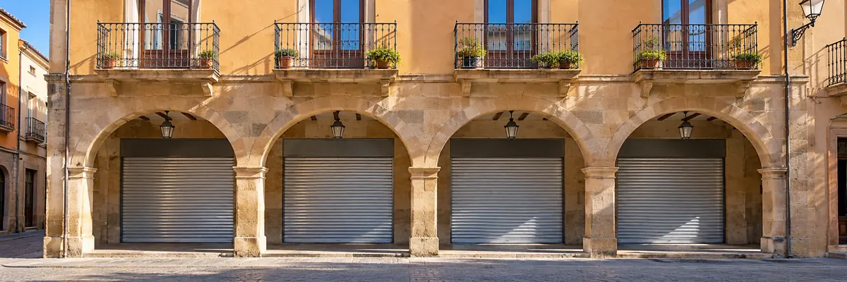 Persianas metálicas galvanizadas bajadas en los bajos comerciales de una calle porticada de Vic